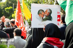 بانویی که عکس شهید نصرالله و شهید سلیمانی را در تشییع پیکر شهید نیلفروشان در دست دارد