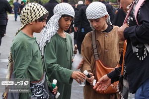 سه پسربچه که با مشک آب از زائران جامانده پیاده روی اربعین پذیرایی میکنند