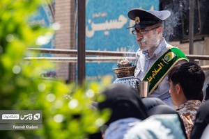 خادم حرم که در مراسم تشییع پیکر مطهر شهید مدافع حرم سعید آبیار در حرم حضرت عبدالعظیم در حال دود کردن اسفند است