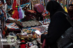 خانمی در حال تماشای زیرانداز های سنتی در نمایشگاه شهرخانواده